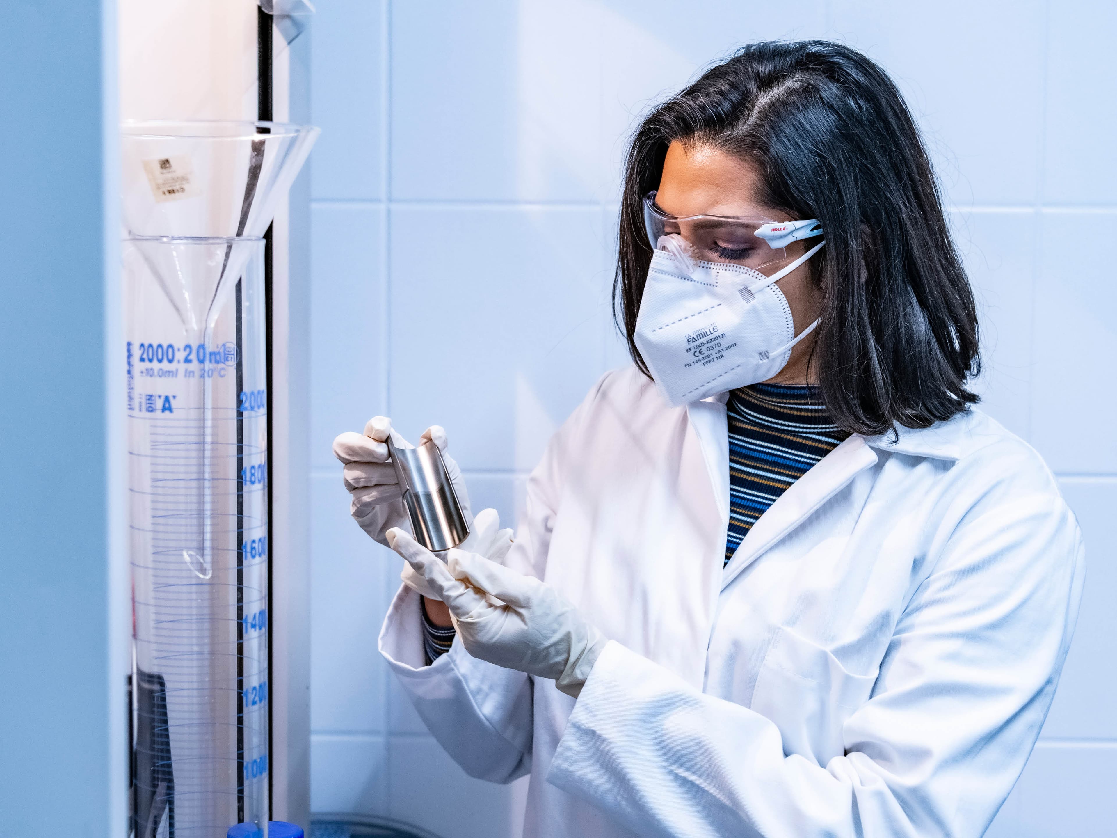 Woman in laboratory wearing protective clothing holding stainless steel half-shell for surface inspection