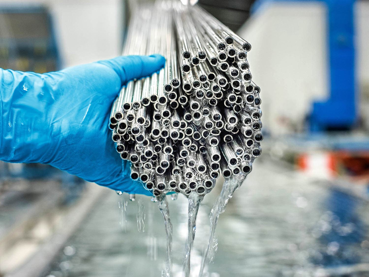 Stainless steel tubes after electropolishing, water rinses through them, a hand on the left steadies the tubes