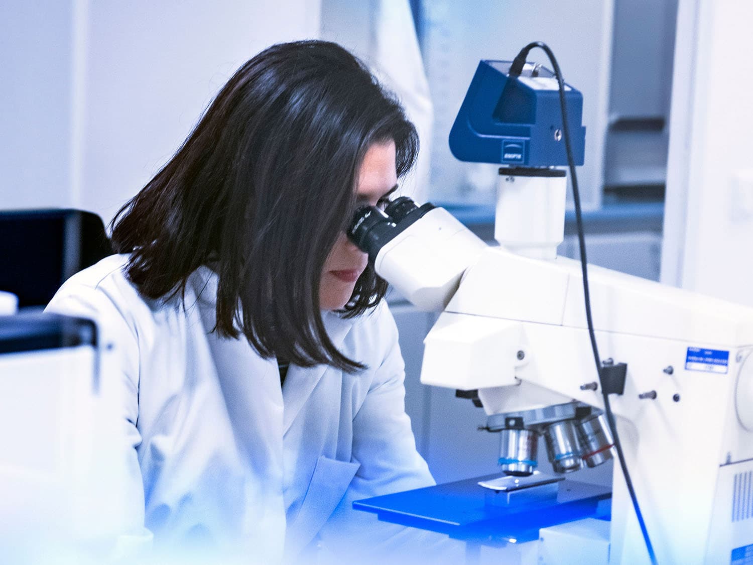 A woman is sitting at a microscope and inspecting a stainless steel component