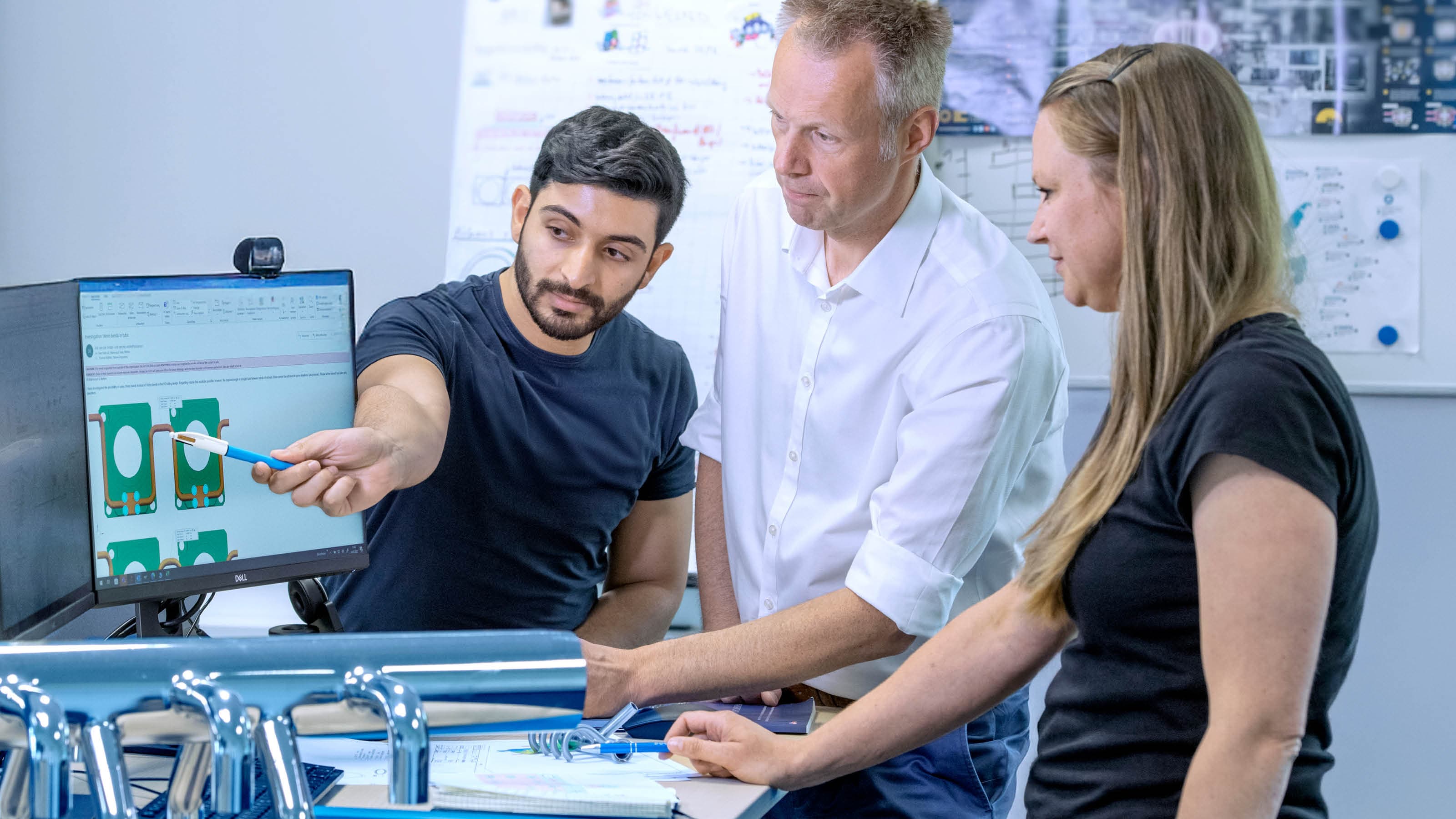 Three employees discuss an application in front of a PC monitor