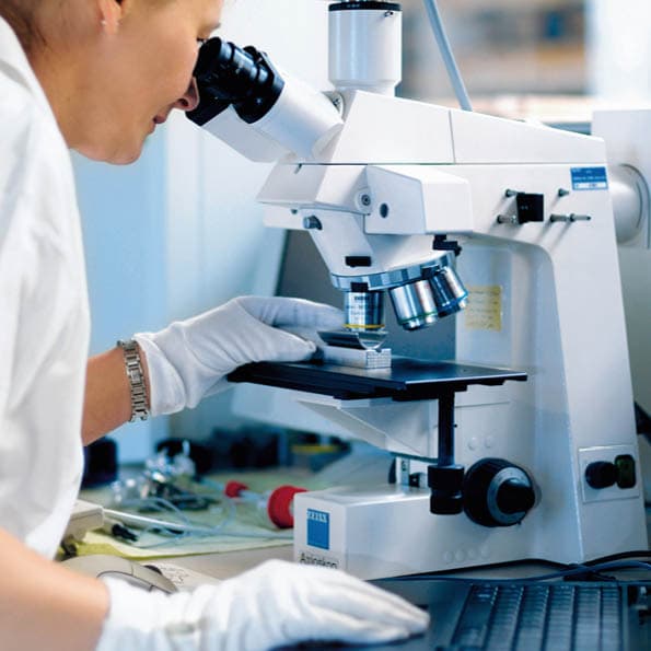 Woman looking through a microscope and inspecting a stainless steel surface