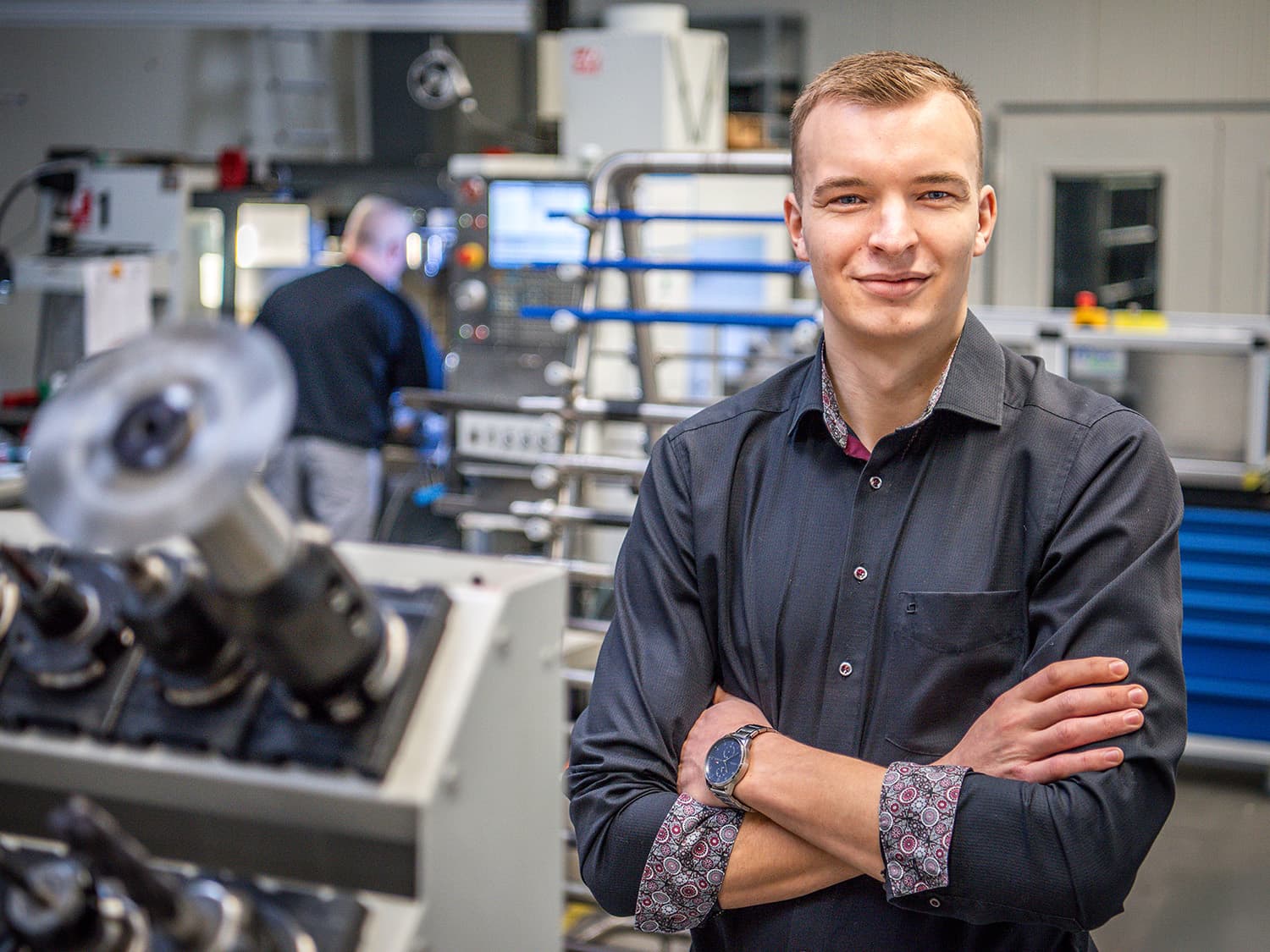 A man is in the foreground of production; a machine can be seen in the background