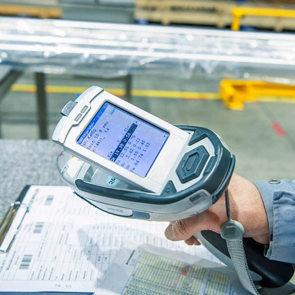 Person holding technical device for material identification; tubes and checklist visible in the background