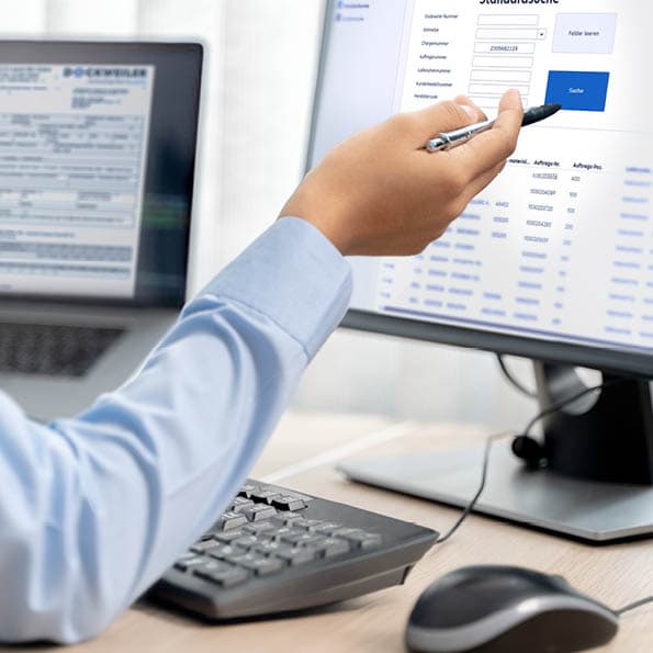 Hand with a pen pointing to a monitor showing the entry mask of the WebCert system