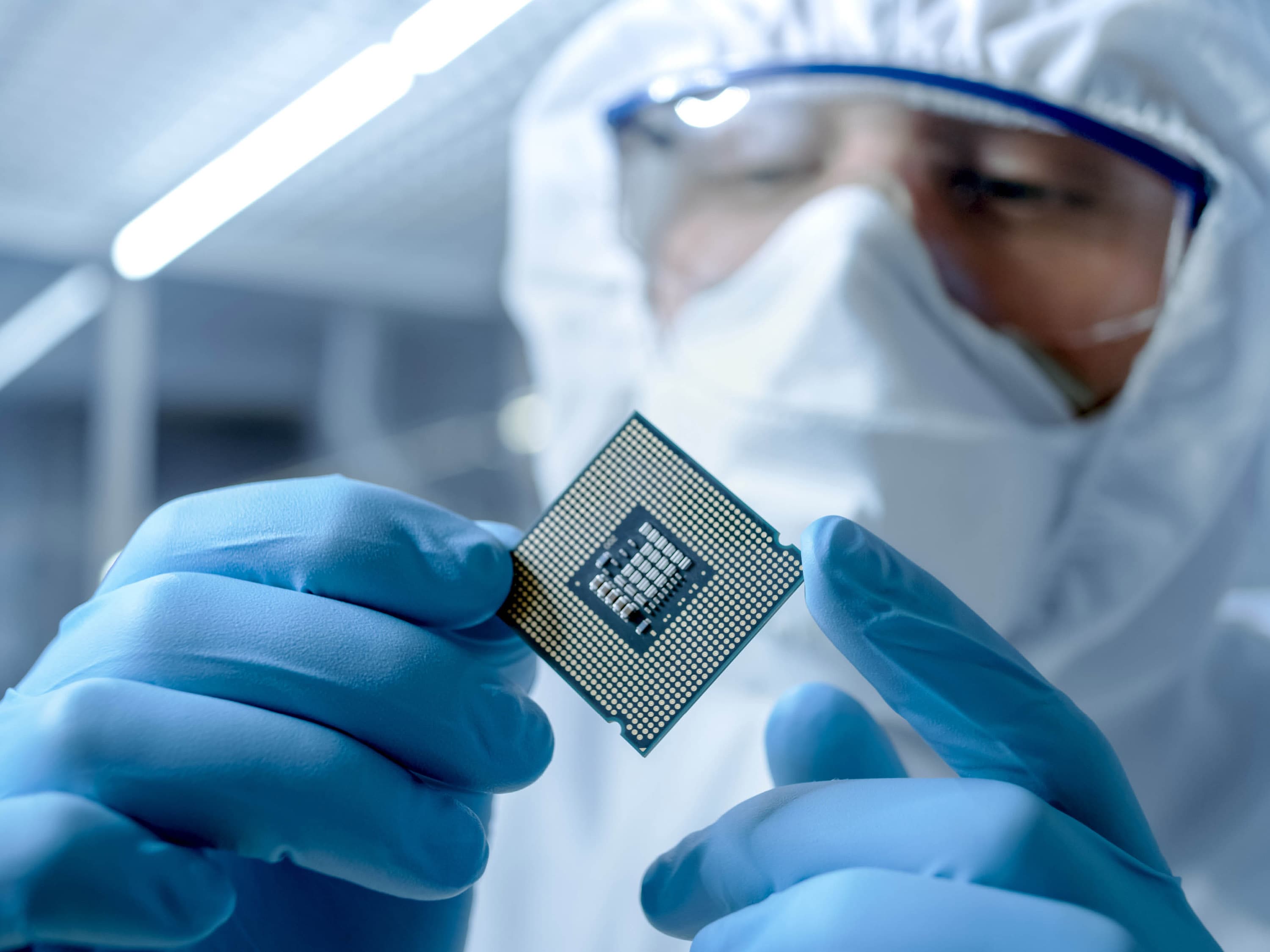 person in cleanroom clothing holds a microchip in their hand