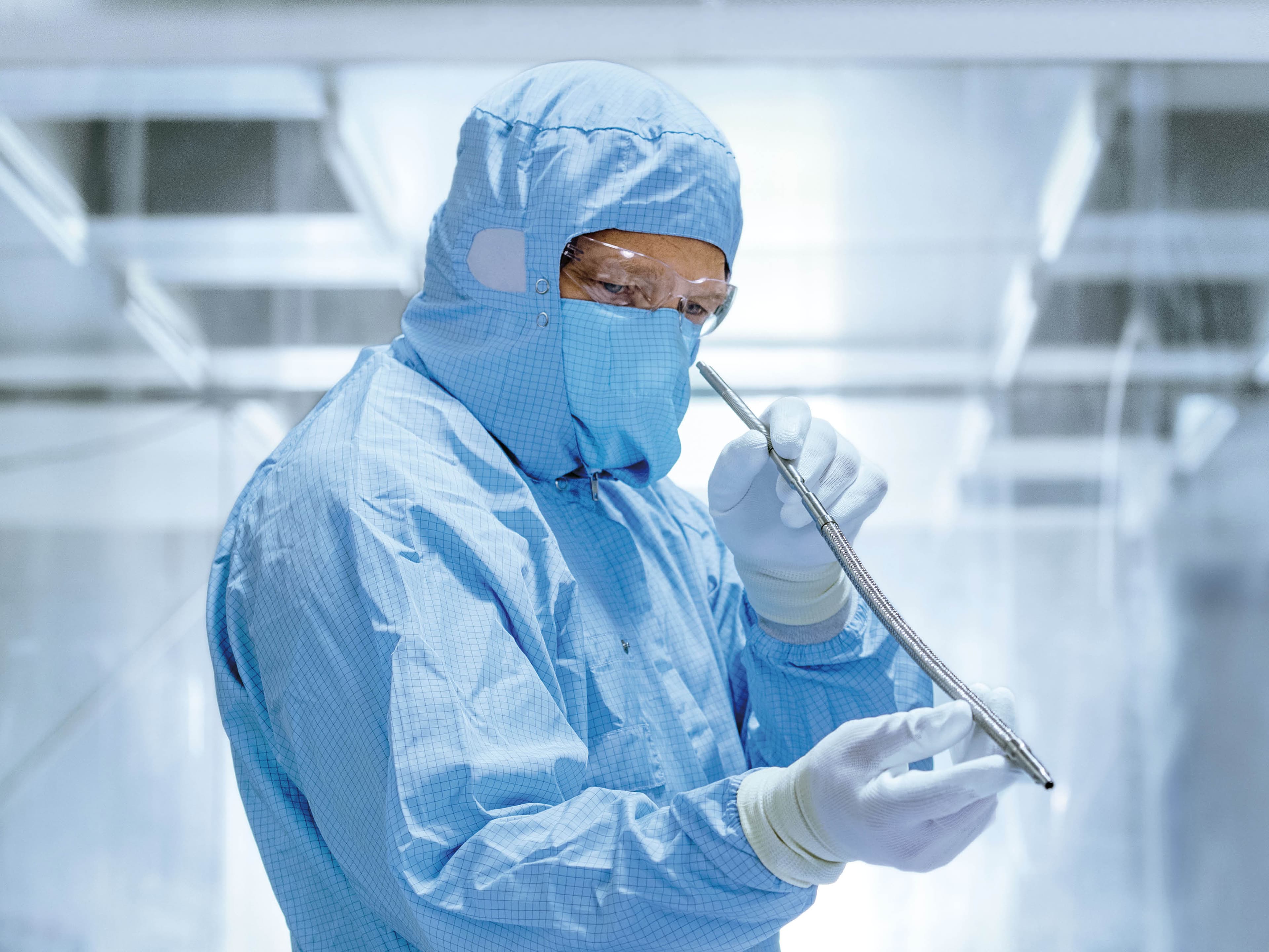 A person in cleanroom clothing is holding a corrugated stainless steel hose in the cleanroom.