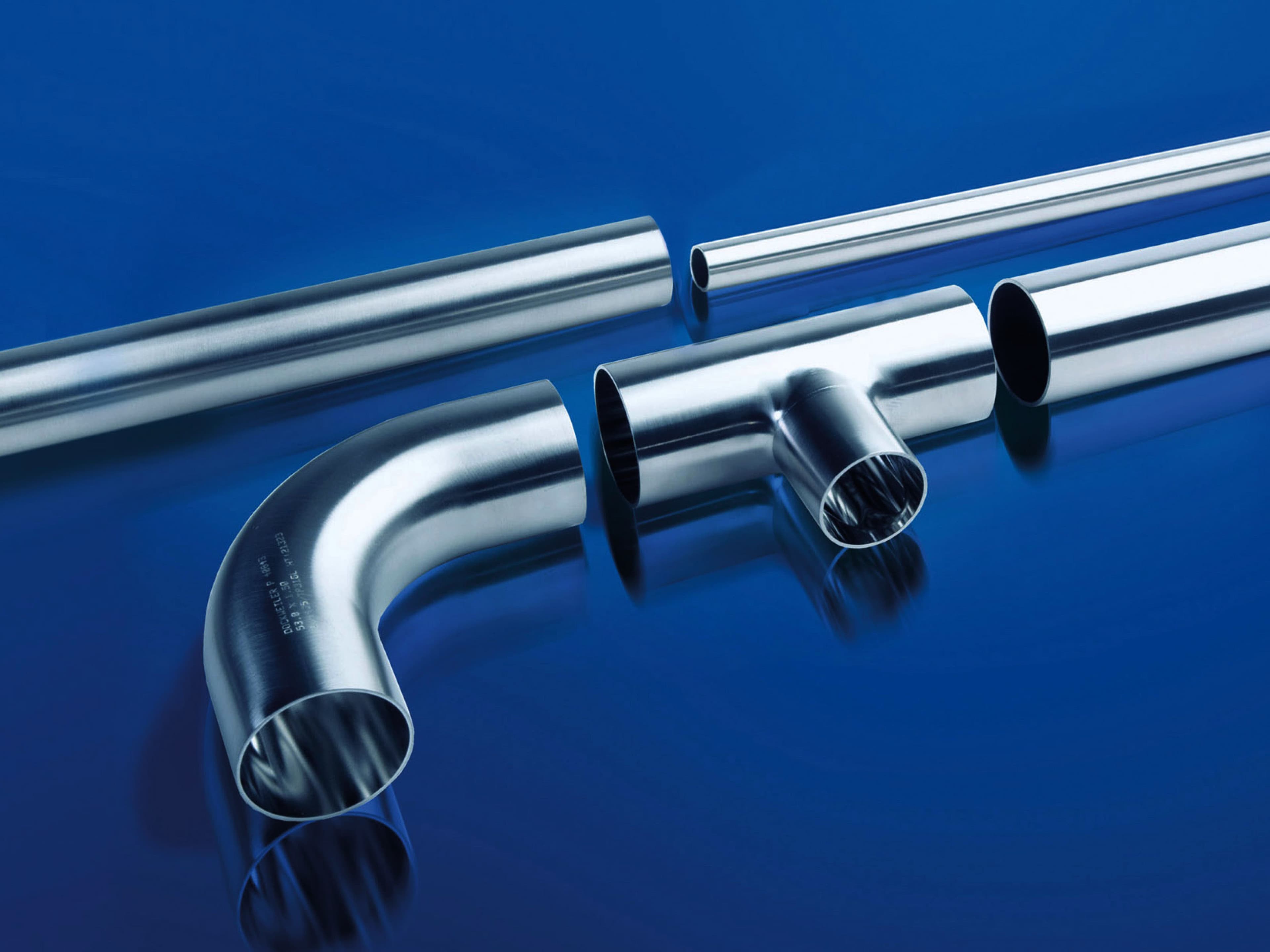 Stainless steel tubes, elbow and T-piece arranged on a blue background
