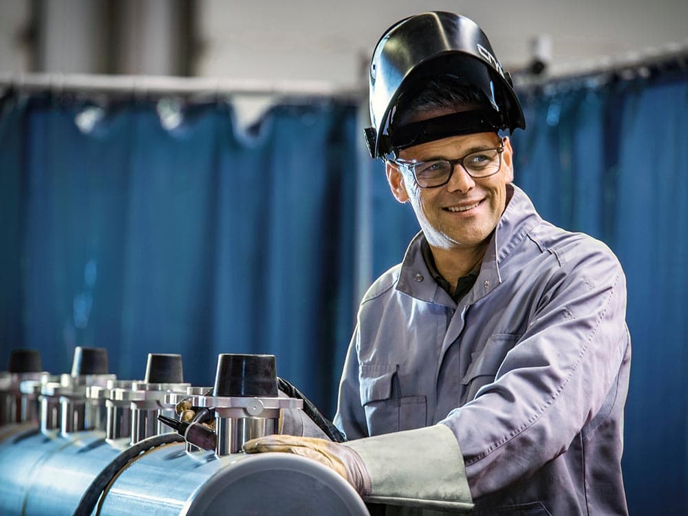 A welder is standing next to a manifold and wearing a welding helmet