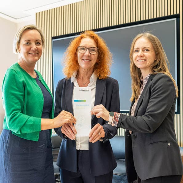 Three female employees hold the company's mission statement in their hands