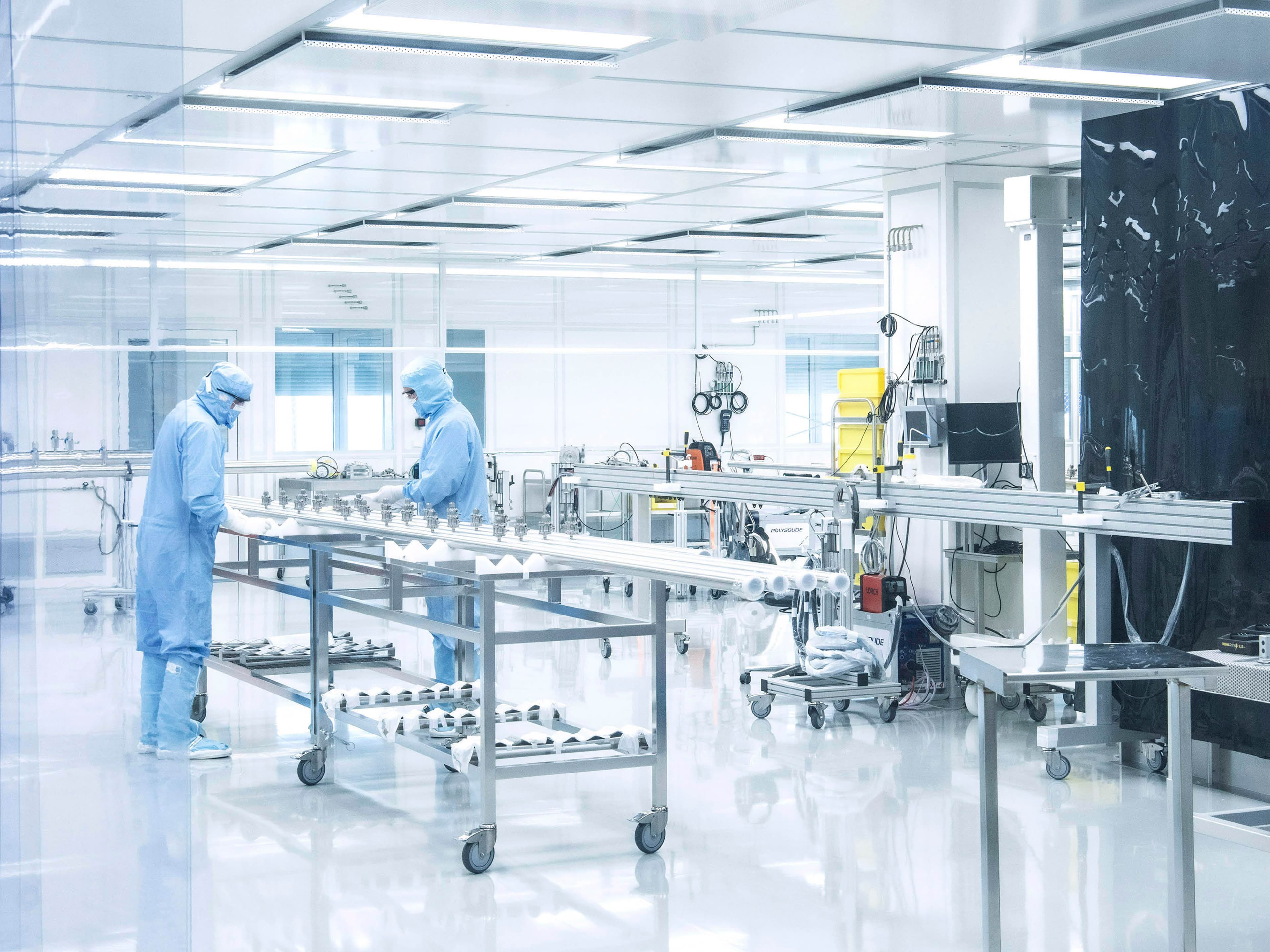 Two employees in protective clothing are working on a manifold in the clean room.