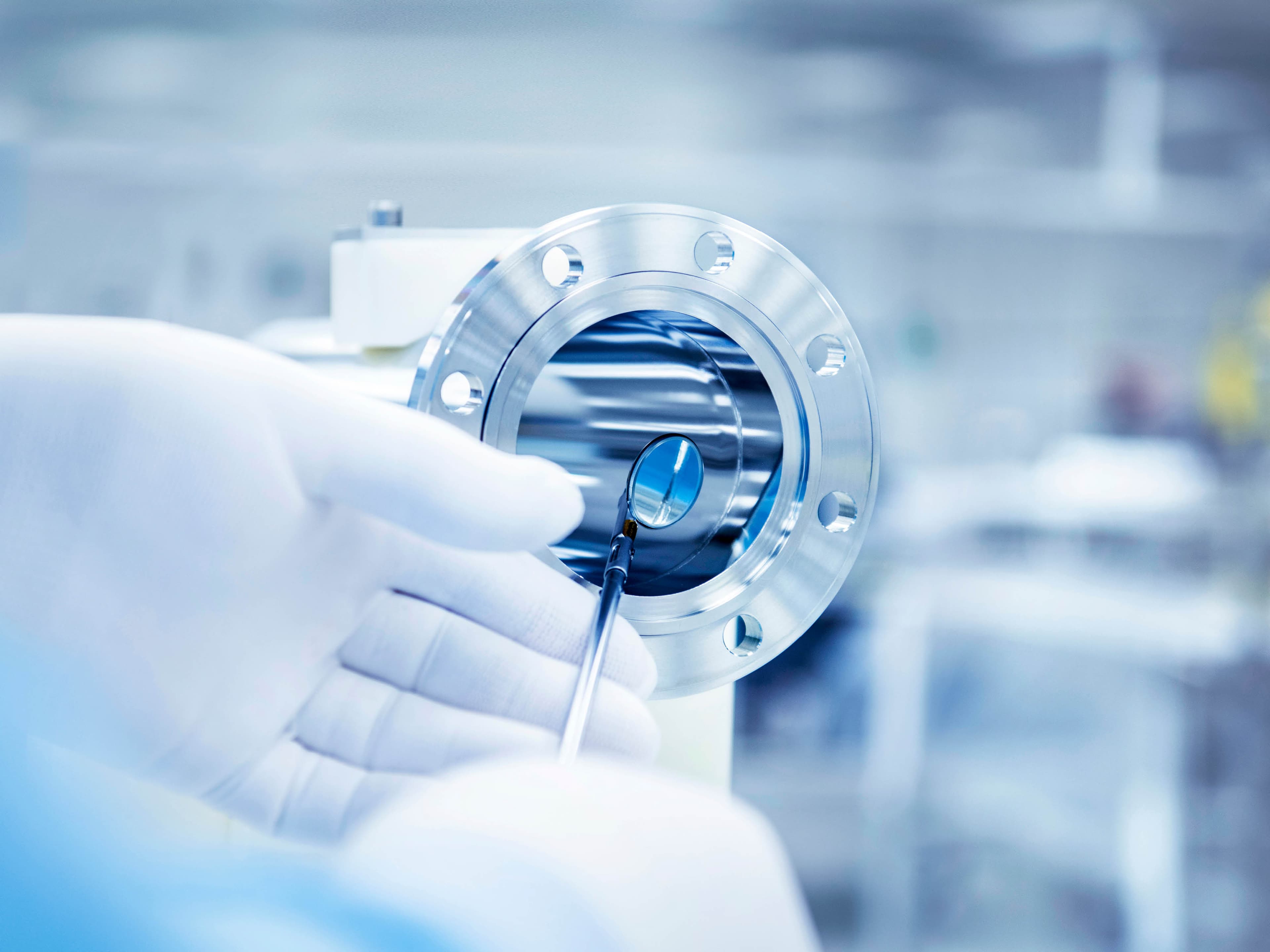 Hands wearing white gloves check a weld on a manifold using a hand mirror; clean room environment