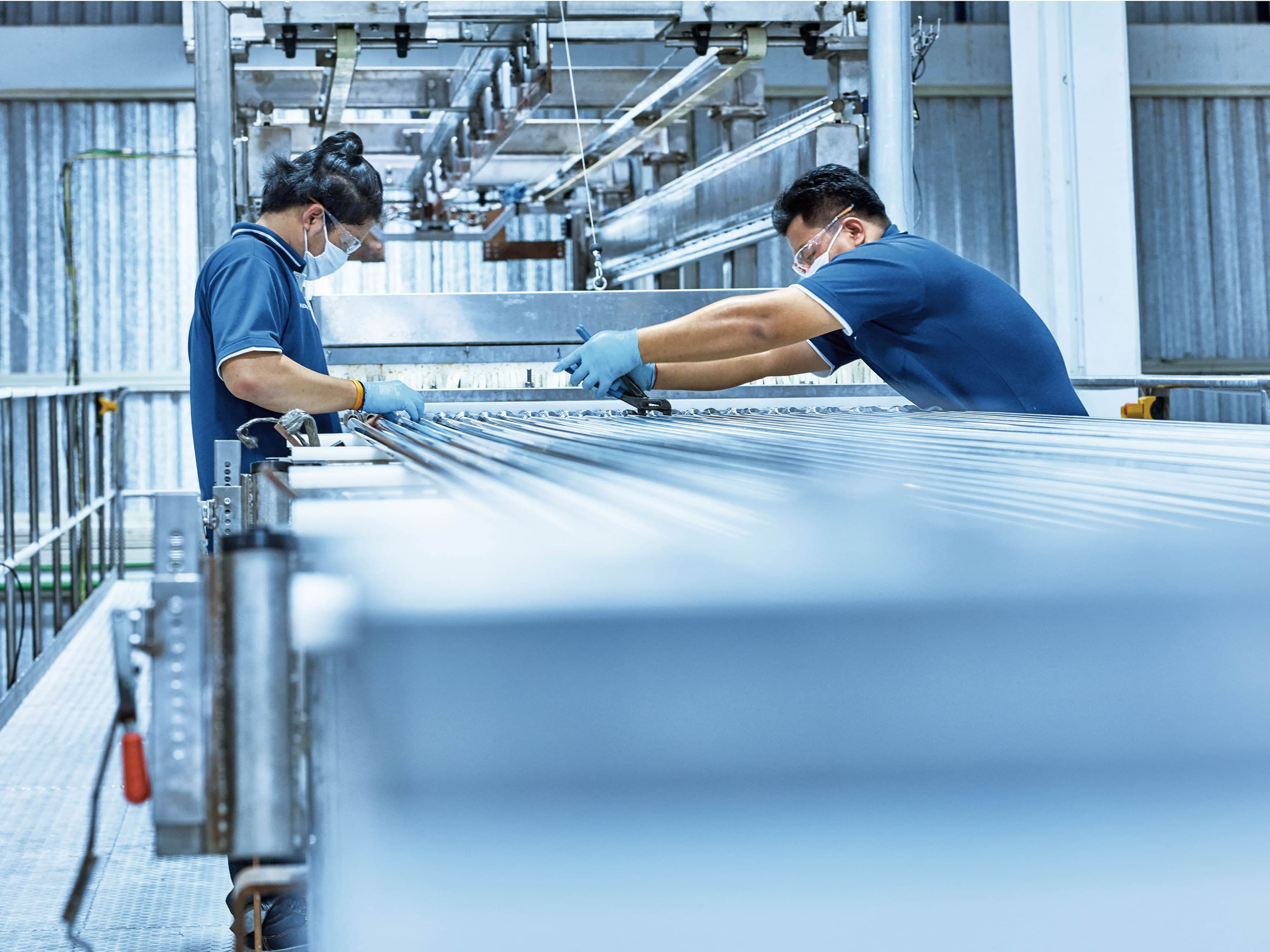 Two employees in protective clothing prepare tubes for electropolishing.