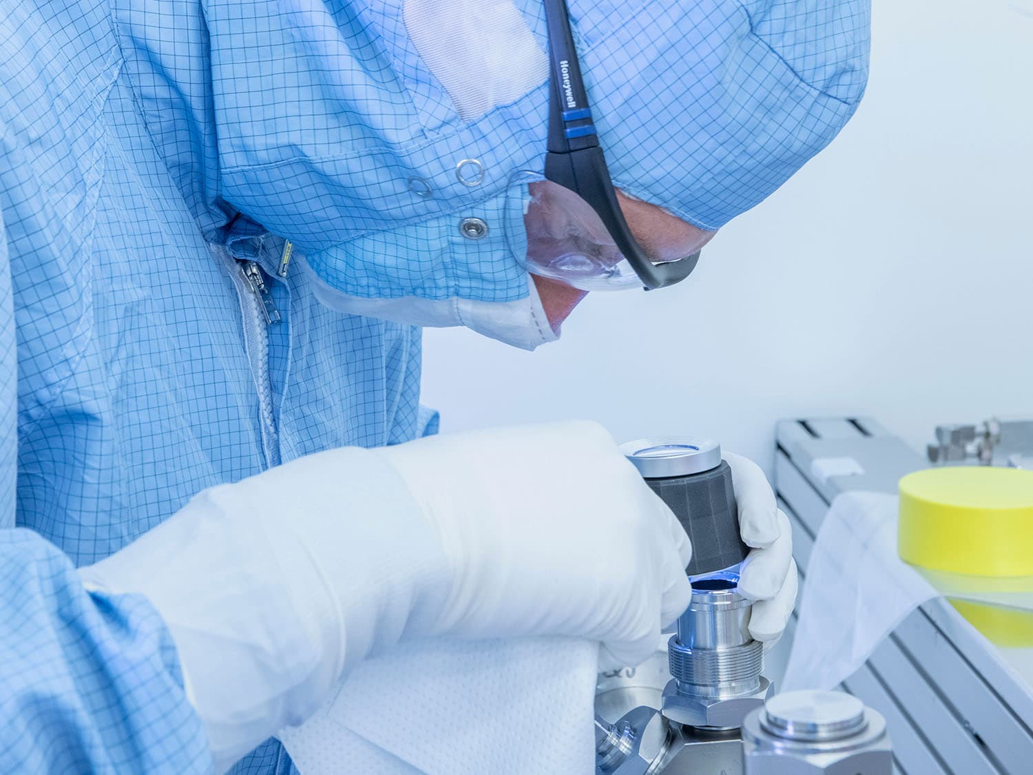 Person in cleanroom clothing checks a component in a cleanroom environment